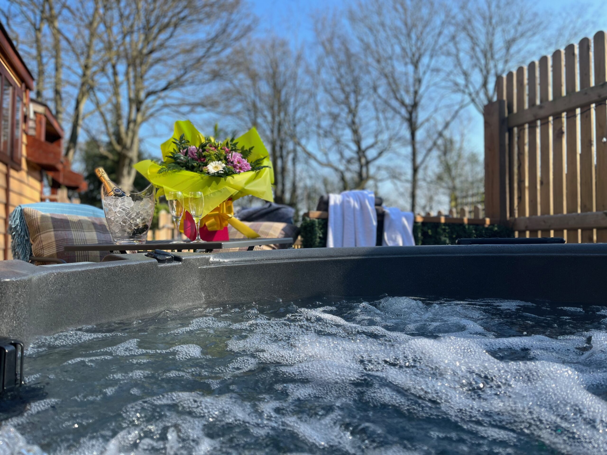 Bubbling hot tub on a sunny day, with champagne on ice and hand-tied bouquet in the background.
